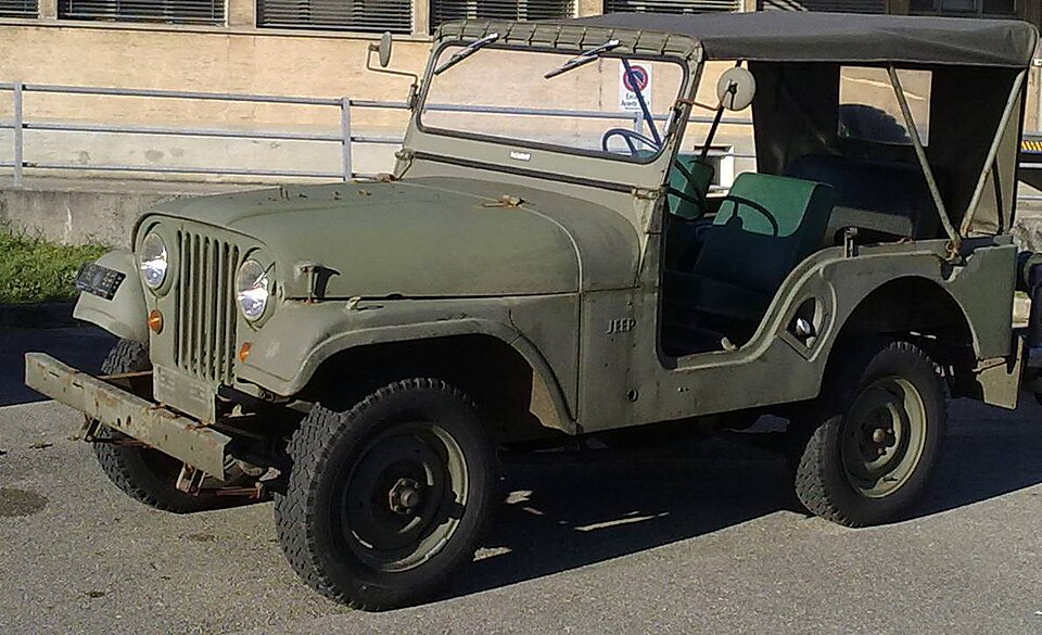 An olive red restored Jeep CJ-5 in front of a simple wooden backdrop
